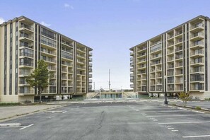 A mid-rise apartment building with multiple balconies, a parking lot, and a clear sky. - Bluewater East 501N (Ocean City)