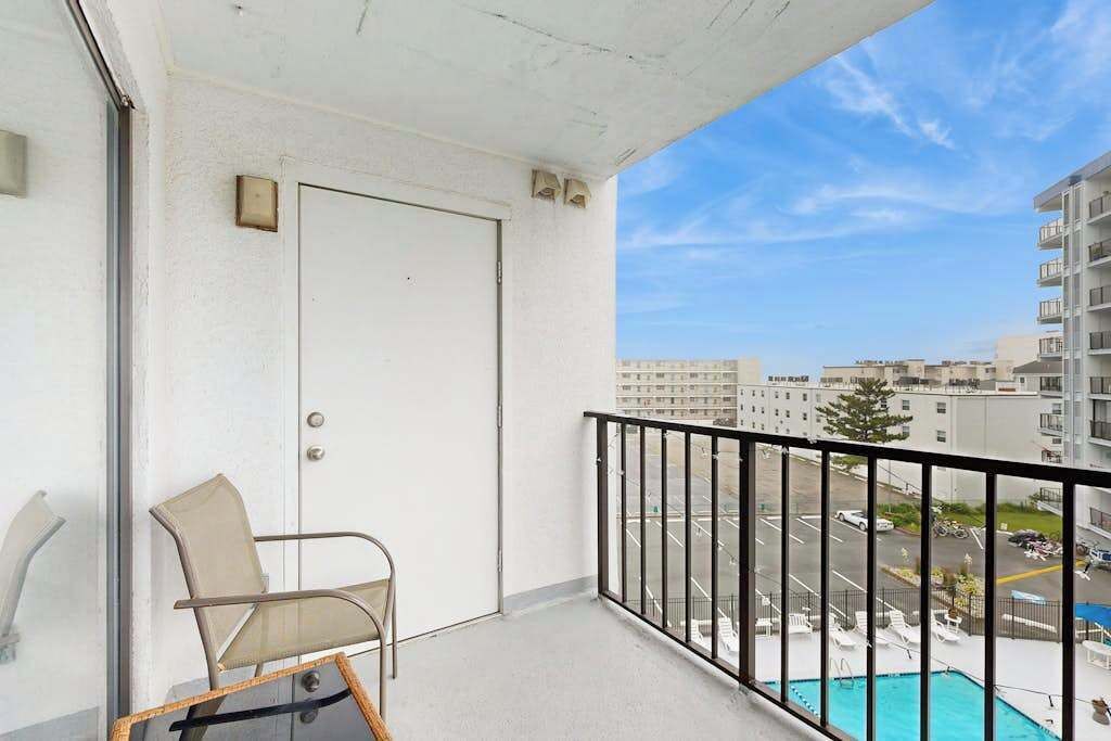 Een balkon met een stoel, een deur en uitzicht op een parkeerplaats en gebouwen.