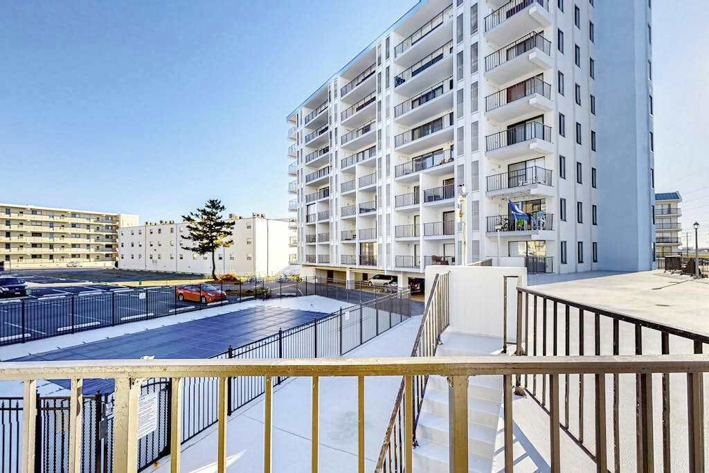 Un hôtel à plusieurs étages, doté de balcons, d’un parking et offrant une vue sur un ciel dégagé.