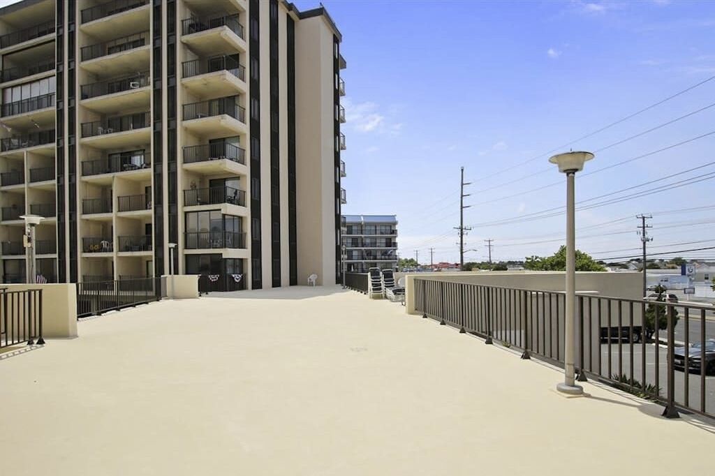 Ein mehrgeschossiges Gebäude mit Balkonen, einer flachen Dachterrasse und blauem Himmel.