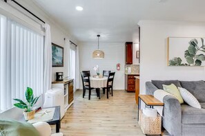 A modern living room with a grey sofa, a dining table with chairs, a coffee machine, and a hanging light fixture. - Oceanside Escape with AC / Walk to Beach, Coffee & Dining (Oceanside)