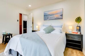 A bedroom with a bed, bedside tables, a nightstand, a door, and a wall-mounted painting. - Oceanside Escape with AC / Walk to Beach, Coffee & Dining (Oceanside)