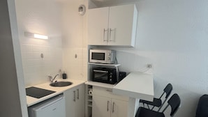 A compact kitchen with white cabinets, a microwave, a sink, and a small dining area with a chair. - Studio in the center of Toulouse, 7 minutes by bike from Place Saint Pierre (Toulouse)