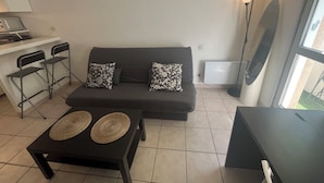 A living area with a sofa, two chairs, a small table with woven placemats, a lamp, and a view through a window. - Studio in the center of Toulouse, 7 minutes by bike from Place Saint Pierre (Toulouse)