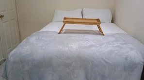 Una cama con cabecera de madera, ropa de cama blanca y una puerta a la izquierda.
