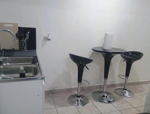 Una kitchenette con un lavabo, un refrigerador pequeño y una silla negra.