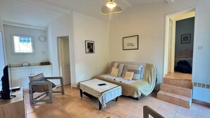 A living room with a sofa, a table, a chair, a hanging light fixture, and a window. - Villa Caroubier - A peaceful stay just a stone's throw from the sea (Zonza)