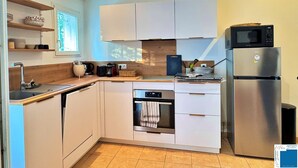 A modern kitchen with white cabinets, a built-in oven, a microwave, and a stainless steel refrigerator. - Villa Caroubier - A peaceful stay just a stone's throw from the sea (Zonza)