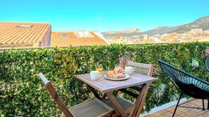 A terrace with a table set for breakfast, including croissants and juice, overlooking a cityscape with buildings and mountains. - Le 6ème Sens: a getaway for two in Toulon (Toulon)