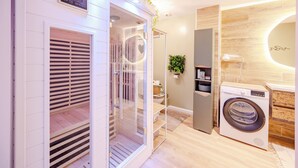 A modern bathroom with a built-in washing machine, a glass shower enclosure, and a digital clock. - Le 6ème Sens: a getaway for two in Toulon (Toulon)