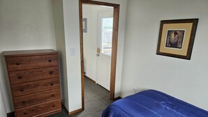 A bedroom with a wooden dresser, a blue bedspread, and a framed picture on the wall.