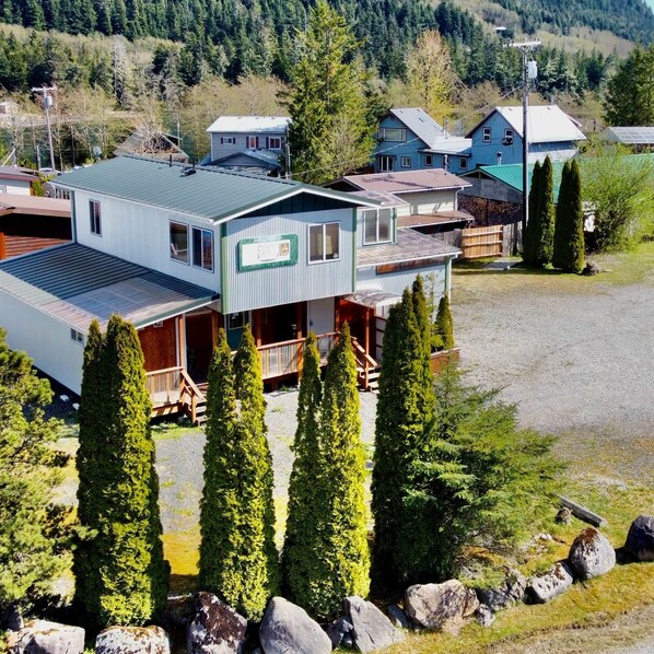 A multi-story building with a covered porch, surrounded by trees and a gravel driveway. - The Queen Mini Suite B (Craig)