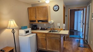 A compact kitchen with wooden cabinets, a microwave, a coffee maker, and a sink. - The Queen Mini Suite B (Craig)
