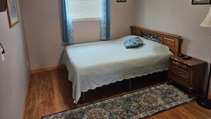 A bedroom with a bed, a nightstand, a lamp, a window with curtains, and a rug. - The Queen Mini Suite B (Craig)