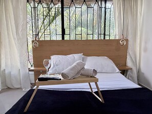 A neatly made bed with white linens, a wooden headboard, and a bedside table with a remote control and glasses. -  Apartaloft Laureles Medellín Wifi  (Medellin)
