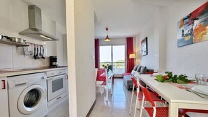 A modern kitchen with a washing machine, a dining area with red chairs, and a view of the outdoors. - Front line duplex - La Arena 4607 (Arnuero)
