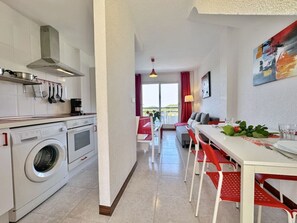 Eine moderne Küche mit Waschmaschine, einem Essbereich mit roten Stühlen und Blick ins Freie.