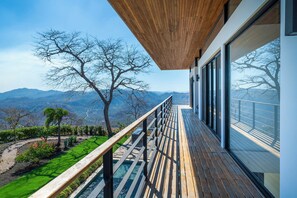 Ein modernes Gebäude mit einer Holterrasse, großen Fenstern und Blick auf Berge.