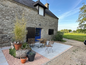 Un bâtiment en pierre avec une porte bleue, des places assises à l’extérieur et un chemin de gravier.