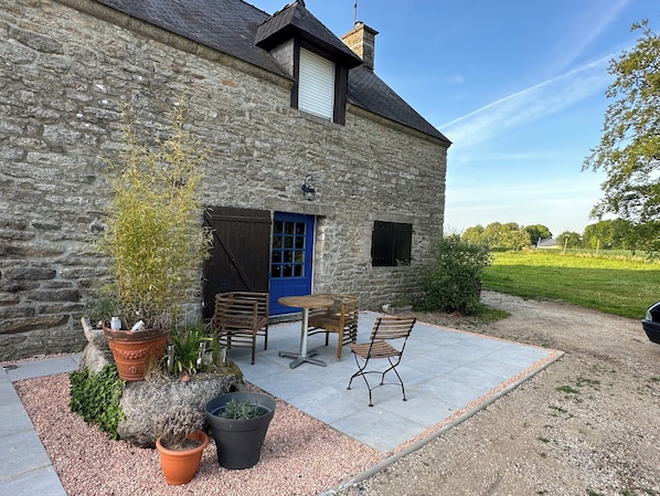 Un bâtiment en pierre avec une porte bleue, des places assises à l’extérieur et un chemin de gravier.