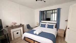 Quarto com cama, escrivaninha, cadeira, televisão e janela com cortinas.