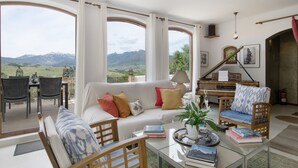 Un ampio soggiorno con una grande finestra, un pianoforte e vista sulle montagne.