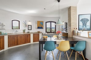 A modern kitchen with wooden cabinets, a dining area with colorful chairs, and a large window with a view. - Dar Hajra, villa para couples with spectacular views of the Sierra de Grazalema (Montecorto)