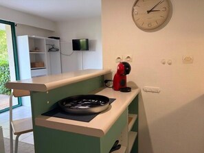A kitchenette with a clock, a TV, and a red appliance on the counter. - Studio with 25 m² terrace & private parking (La Rochelle)