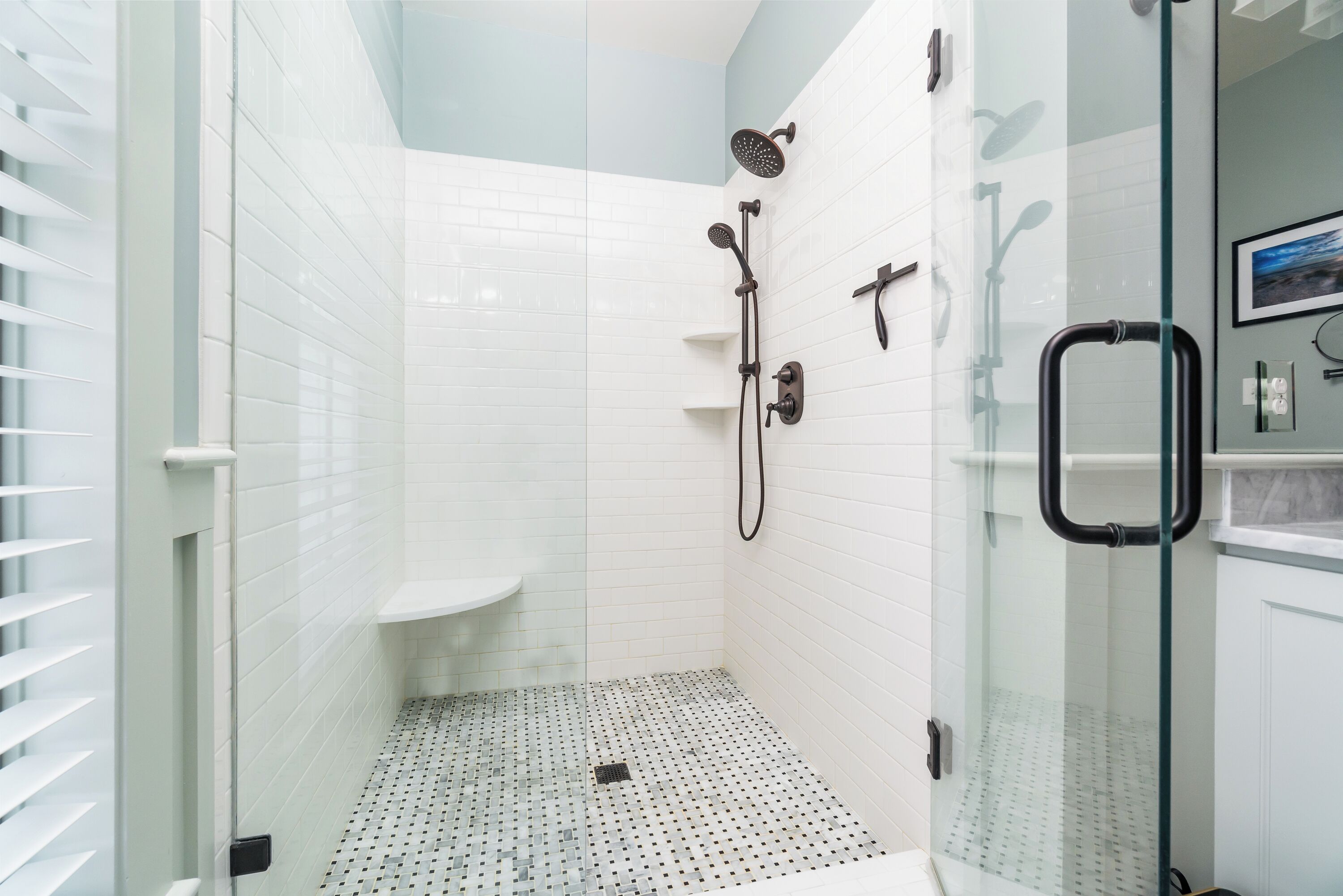 Una ducha con cerramiento de vidrio, paredes de azulejos blancos y piso con diseño.