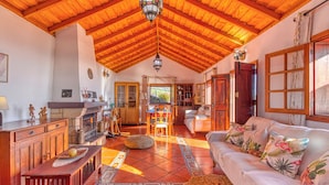 A spacious living area with a high wooden ceiling, a fireplace, a sofa with tropical pillows, and a dining area with a table and chairs. - Casa El Algarrobo – Home above the clouds with sea views (Puntagorda)