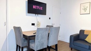 Uma sala de estar moderna com área de jantar, TV de tela plana na parede, sofá e um quadro pendurado na parede.
