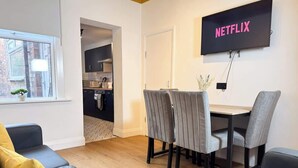 Uma sala de estar moderna com área de jantar, TV fixada na parede e vista para a cozinha.