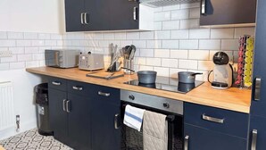 Uma cozinha moderna com armários escuros, bancada de madeira, forno embutido e diversos eletrodomésticos.