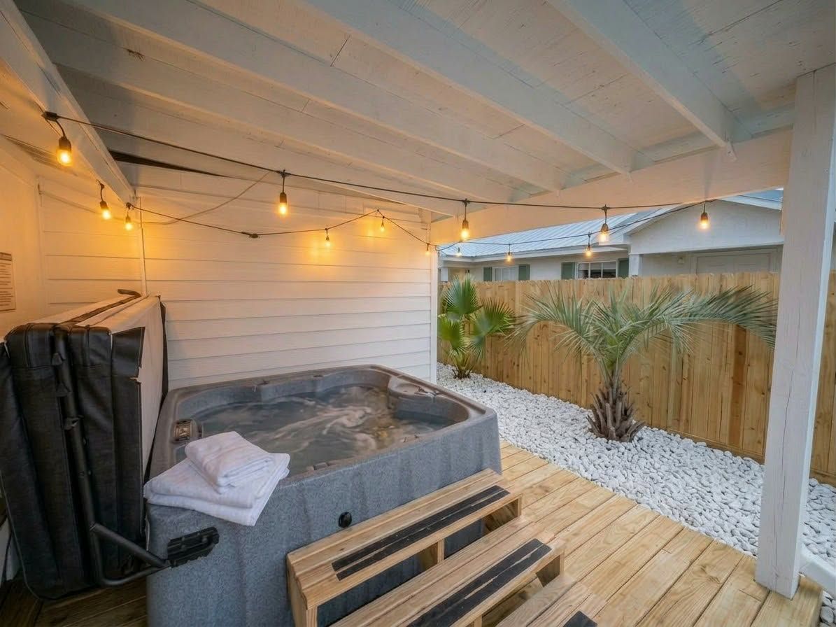 A hot tub on a wooden deck with string lights overhead.