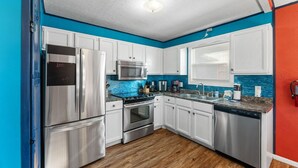 A modern kitchen with stainless steel appliances, white cabinets, and a blue accent wall. - Pool/Hot Tub/Golf Cart + 3 Min Stroll to Beach (Panama City)