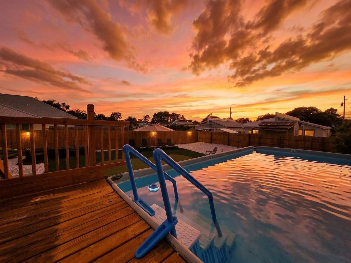 Une piscine avec une terrasse en bois et un coucher de soleil en arrière-plan.