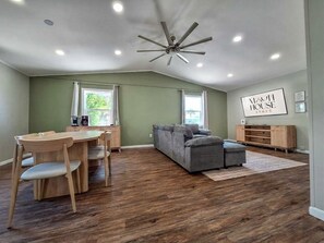 A spacious living area with a dining table, a sofa, and a ceiling fan.