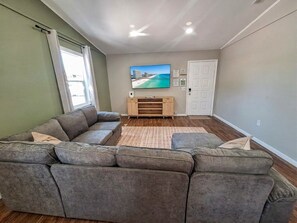 A living room with a sectional sofa, a flat-screen TV mounted on the wall, a wooden entertainment unit, and a door.