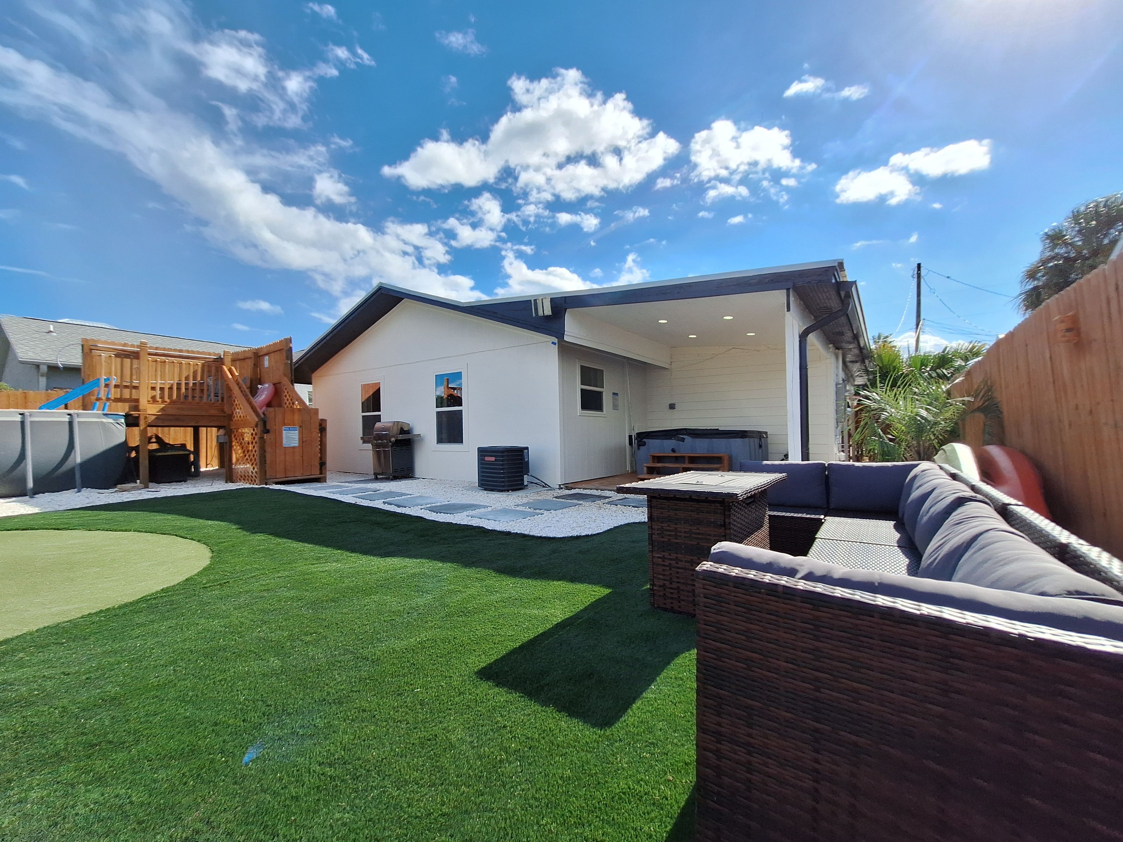 Un jardin avec une pelouse artificielle, une structure de jeu en bois, un barbecue et un jacuzzi.