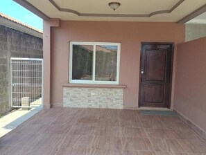 Una habitación con suelo de baldosas, ventana con vistas, una puerta y una lámpara fijada a la pared.