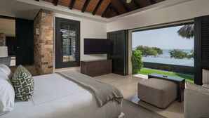 Quarto com uma cama grande, televisão, parede de pedra e vista para o mar.
