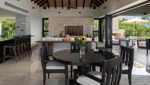 Uma cozinha moderna com lareira, área de jantar com mesa redonda e cadeiras, e área de estar ao ar livre com guarda-sóis.