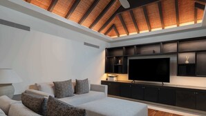 Uma sala de estar moderna com uma grande TV de tela plana, um móvel embutido preto para entretenimento e um teto inclinado com vigas aparentes.