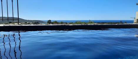 A clear view of a swimming pool with a metal frame, calm water, and a distant landscape with buildings and hills.