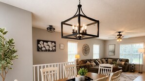 A dining area with a wooden table and white chairs, a chandelier, and a living room in the background. - Family Retreat Near Randolph AFB, Patio & Comfort (Converse)