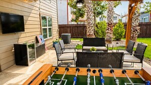 An outdoor patio with a foosball table, seating area, and a TV mounted on the wall. - Family Retreat Near Randolph AFB, Patio & Comfort (Converse)