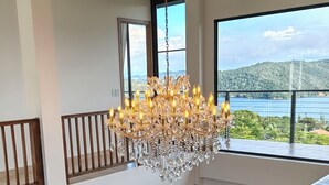 Un interior de varios niveles con una araña, barandillas de madera y grandes ventanales que ofrecen vistas a un cuerpo de agua y colinas.