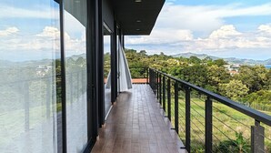 Un balcón con piso de madera, ventanas amplias y vistas a un paisaje montañoso.