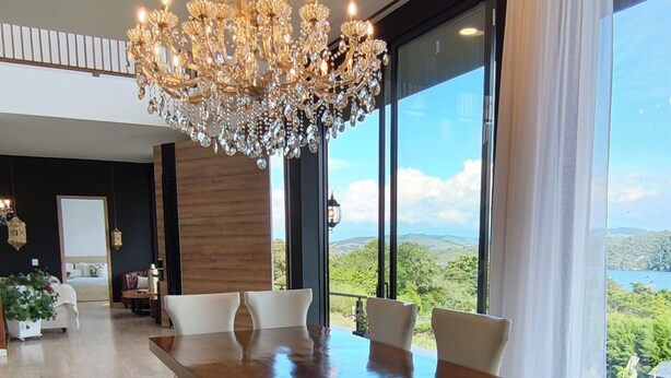 Un comedor moderno con una gran mesa de madera, sillas blancas tapizadas y una araña.