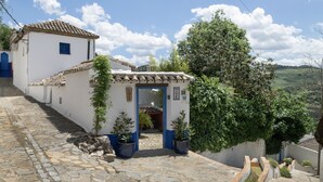 A white building with a tiled roof, a cobblestone path, and potted plants.